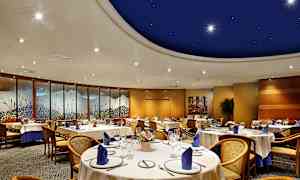 Ett elegant inredd matsal med runda bord och stolar, dekorerad med blå servetter och konstverk längs väggarna. (AI-genererad text)