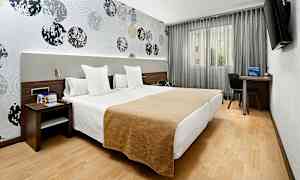 Ett hotellrum med två enkelsängar placerade bredvid varandra. Väggarna är dekorerade med ett mönster av cirklar, och det finns en tv, skrivbord och stol vid fönstret. (AI-genererad text)