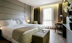 Ett hotellrum med två sängar, skrivbord och stora fönster. (AI-genererad text)