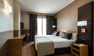 Ett hotellrum med två enkelsängar som står ihop, ett skrivbord med stol och en väggmonterad TV. (AI-genererad text)