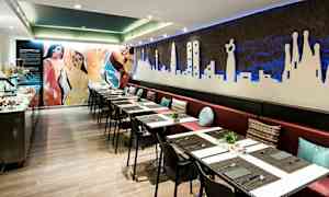 En restaurang med lång bänk och bord med dukar samt dekorationer på väggarna. (AI-genererad text)