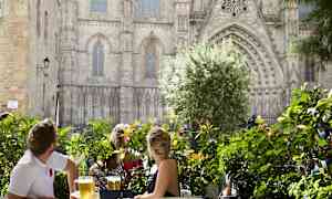 Människor sitter vid ett bord omgivna av grönska med en storslagen byggnad i bakgrunden. (AI-genererad text)