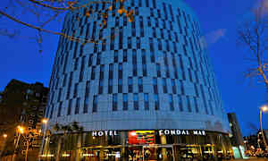 Ett hotell med modern arkitektur och fasad i ränder av glas och betong fotograferat i skymningen. (AI-genererad text)