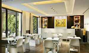 Ett modernt kafé med vita bord och stolar framför en bar i en ljus interiör. (AI-genererad text)