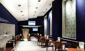 En modern restaurang eller café med trämöbler och mörk dekor. Det visar bord och stolar arrangerade i rader under ett starkt upplyst tak. (AI-genererad text)