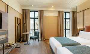 Ett modernt hotellrum med två sängar, ett bord med en stol framför stora fönster och golv i trä. (AI-genererad text)