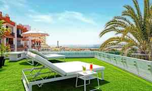 Takterrass med gräsmatta, solstolar, ett litet bord med drycker och utsikt över omgivningar. (AI-genererad text)