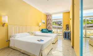 Ett hotellrum med två enkelsängar, en blå soffa och stora fönster med utsikt utanför. (AI-genererad text)