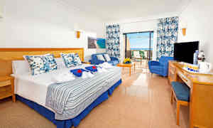 Ett hotellrum med en dubbelsäng, sittgrupp och uteplats. Utsikten visar havet. (AI-genererad text)