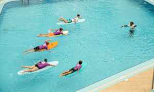 En grupp människor ligger på surfbrädor i en pool, och en instruktör står i vattnet. (AI-genererad text)