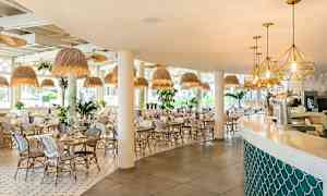 Bild av en ljus och modern restaurang med vita stolar och bord, taklampor i naturnära stil, samt en bar med mjuka linjer. (AI-genererad text)