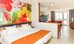 Hotellets rum med säng, färgglad väggmålning av blommor och sittgrupp med kök. (AI-genererad text)