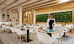 En restaurang med modern inredning med vita stolar, dukade bord och en vägg dekorerad med växter. (AI-genererad text)