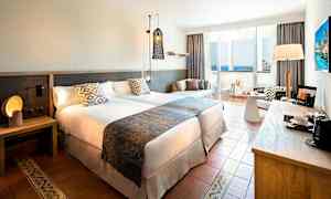 Hotellrum med två sängar, nattduksbord, sittgrupp och balkong med havsutsikt. (AI-genererad text)