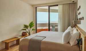 Ett ljust och modernt inrett hotellrum med en stor säng och en balkong som har utsikt över havet. (AI-genererad text)