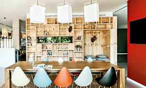 Ett rum med ett stort träbord och färgglada stolar, omgiven av trähyllor fyllda med böcker och dekorationer. (AI-genererad text)