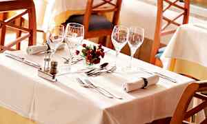 Ett dukat bord med vita dukar, glas, bestick, servetter och en liten blomdekoration. (AI-genererad text)