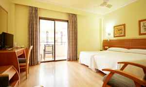 Ett ljust hotellrum med två sängar, skrivbord, stol, och balkong med glasdörrar. (AI-genererad text)