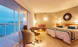 Ett hotellrum med två sängar, en sittgrupp och en utsikt över en balkong med utsikt över staden. (AI-genererad text)