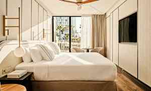 Ett modernt hotellrum med en stor säng, två fåtöljer framför fönstret och en takfläkt. (AI-genererad text)