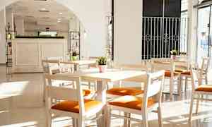 Ljusa trämöbler med orange sittdyna i ett solbelyst rum med stora fönster. (AI-genererad text)