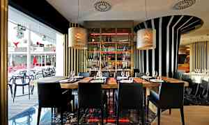 Interiör av en modern restaurang med träbord och svarta stolar, omgiven av randiga väggdekorationer och stora fönster. (AI-genererad text)