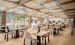 En restaurang med bord och stolar i trä, väl upplyst med naturligt ljus. (AI-genererad text)