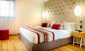 Ett sovrum med en stor säng, prydnadskuddar och en färgmatchad sängduk. På väggen bakom sängen finns dekorativa detaljer, och till höger står ett nattduksbord. (AI-genererad text)