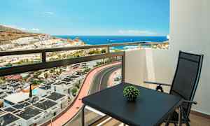Utsikt från en balkong mot havet, med ett bord och en stol. (AI-genererad text)