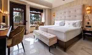 Hotellrum med två bäddar, sittmöbler och utsikt mot trädgård. (AI-genererad text)