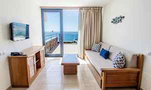 Ett hotellrum med sittgrupp och utsikt mot havet från en balkong. (AI-genererad text)