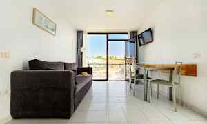 Ett vardagsrum med en mörk soffa, ett matbord med stolar och en balkong med utsikt. (AI-genererad text)