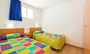 Ett rum med två enkelsängar täckta med färgglada mönstrade överkast. (AI-genererad text)