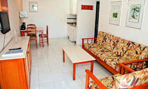 Ett vardagsrum med en soffa med blomstrad klädsel, ett soffbord, en köksyta och en matplats med stolar. (AI-genererad text)