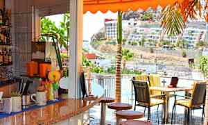 Ett kafé med utsikt över en solig väg och byggnader. (AI-genererad text)