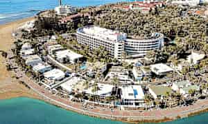 Flygbild av en kuststad med hotell, palmer och strand. (AI-genererad text)