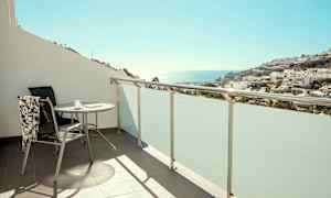 Balkong med bord och stol, utsikt mot hav och bebyggelse. (AI-genererad text)