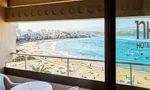 Utsikt från en balkong mot en sandstrand och stad med klart blått hav. (AI-genererad text)