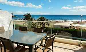 En möbelgrupp på en balkong med utsikt över stranden och havet. (AI-genererad text)