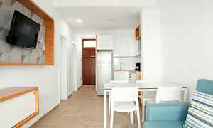 Ett modernt kök och vardagsrum med ljus inredning, vitmålade väggar och en blå soffa. (AI-genererad text)