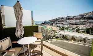 Balkong med utsikt över en strand och bergtäckt med byggnader. (AI-genererad text)