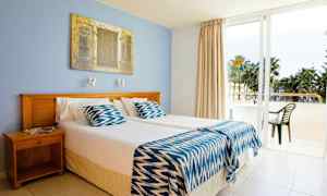 Ett hotellrum med två enkelsängar, en blå vägg och en glasdörr som leder ut till balkongen. (AI-genererad text)