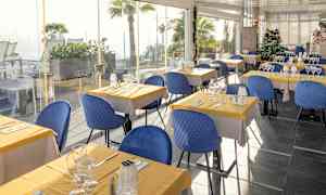 Restaurang med bord dukade med gula dukar och blå stolar. (AI-genererad text)