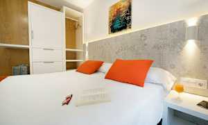 Sovrum med vit dubbelsäng, orange kuddar och öppet klädskåp. (AI-genererad text)
