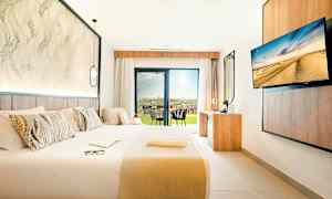 Modern hotellrum med stor säng, skrivbord och utsikt mot en terrass. (AI-genererad text)