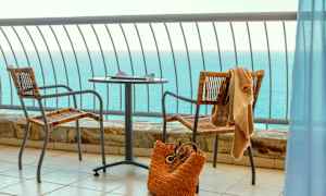 Utsikt över havet från en balkong med bord, två stolar och en strandväska. (AI-genererad text)