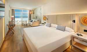 Ett hotellrum med en stor säng, soffa och utsikt över havet genom fönster. (AI-genererad text)