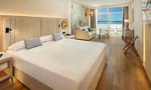 Hotellrum med stor säng, sittgrupp och balkong med havsutsikt. (AI-genererad text)