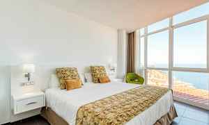 Ett hotellrum med en bäddad säng, stora fönster och utsikt över havet. (AI-genererad text)