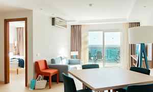 Ett hotellrum med sittgrupp, matbord och havsutsikt från balkongen. (AI-genererad text)